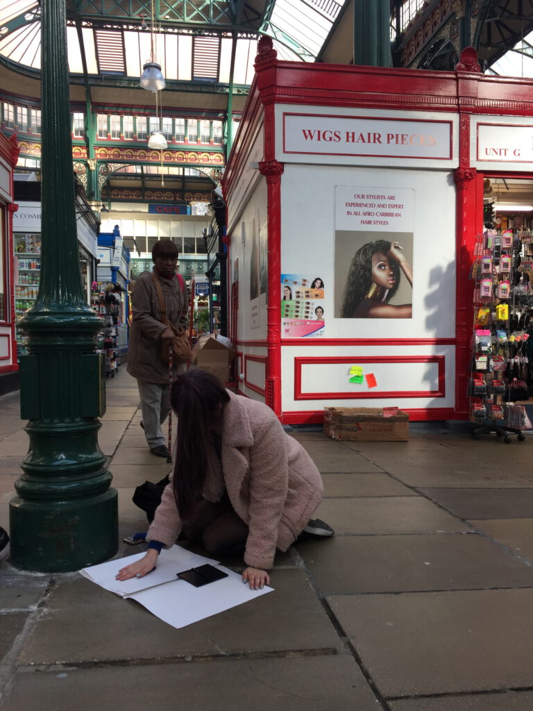 Studentin aus Leeds macht einen Stempeldruck auf Papier auf dem Boden der Markthalle.