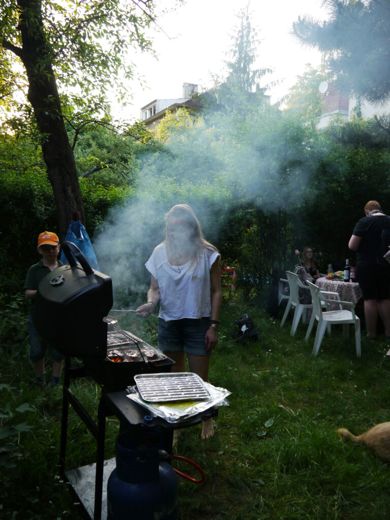 Frau am Grill, von Rauch. verdeckt. Szene im Garten am frühen Sommerabend