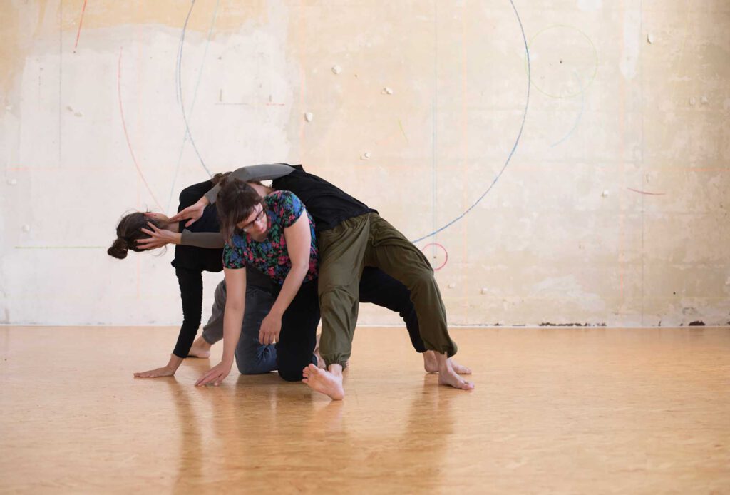 Drei Menschen Tanzen Contact Improvisation vor einer Wand.
